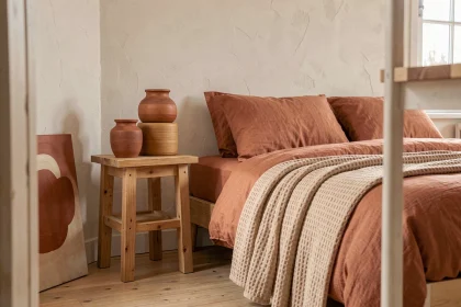 Chambre décorée dans des tons terracotta avec linge de lit en lin rouille, vases en céramique ocre et parquet en chêne brut