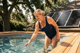Femme testant l'eau chauffée d'une piscine équipée d'un système de chauffage solaire en fin de saison